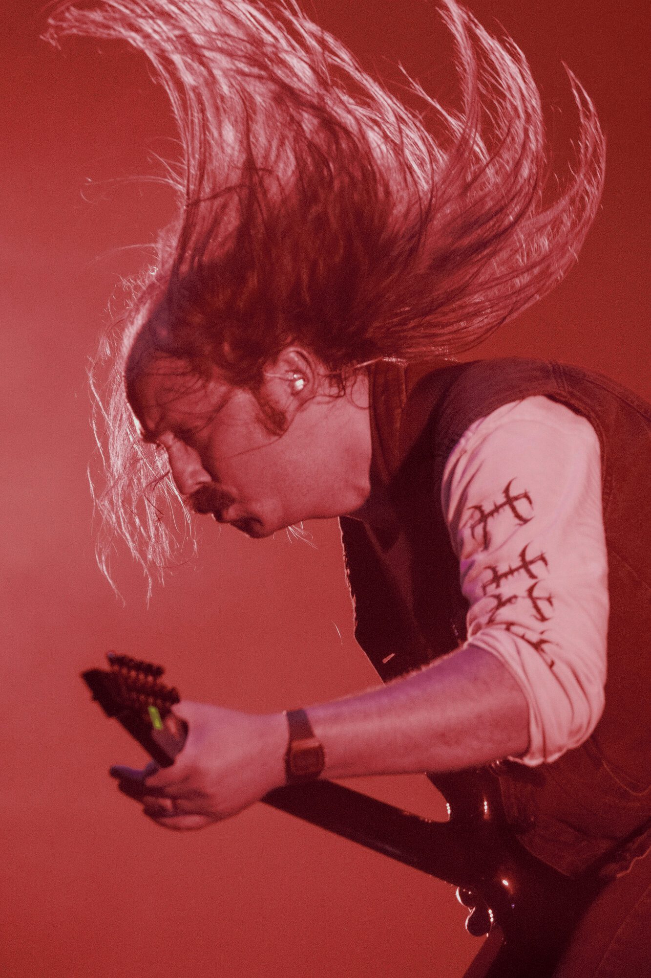 Guitarrista con el cabello en el aire a medio headbang, iluminado desde atrás